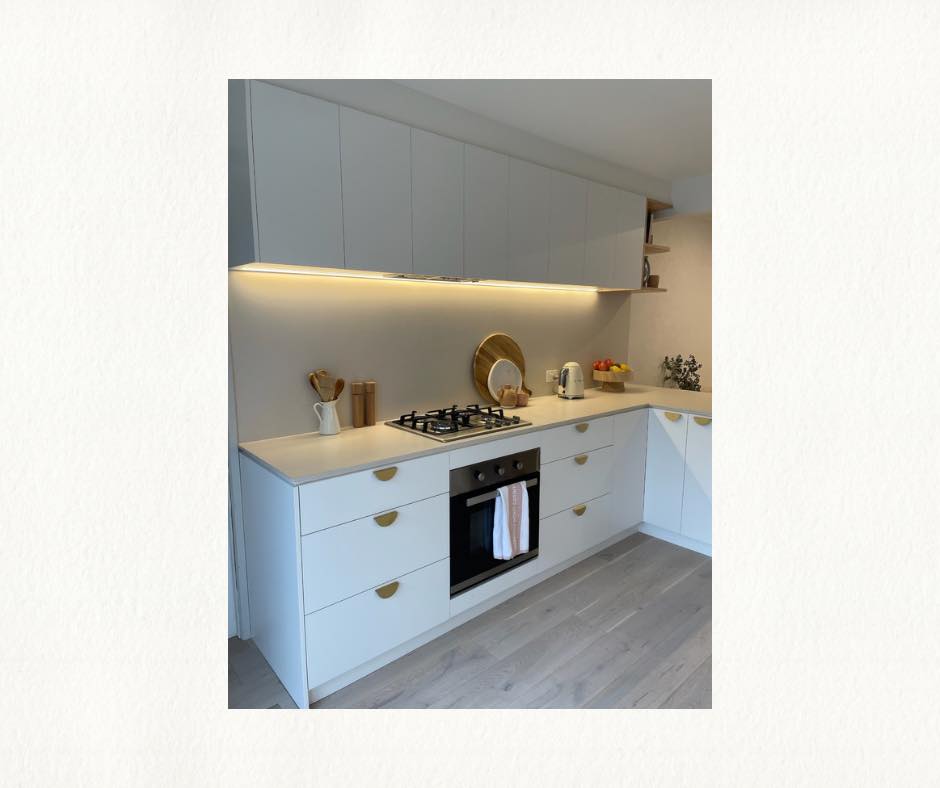 White kitchen cabinetry with brass finishings and an oven with a gas stove top above