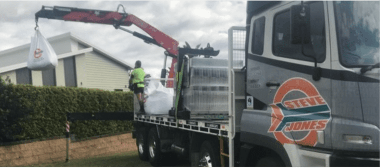 Steve jones delivery truck with crane delivering over residential hedges