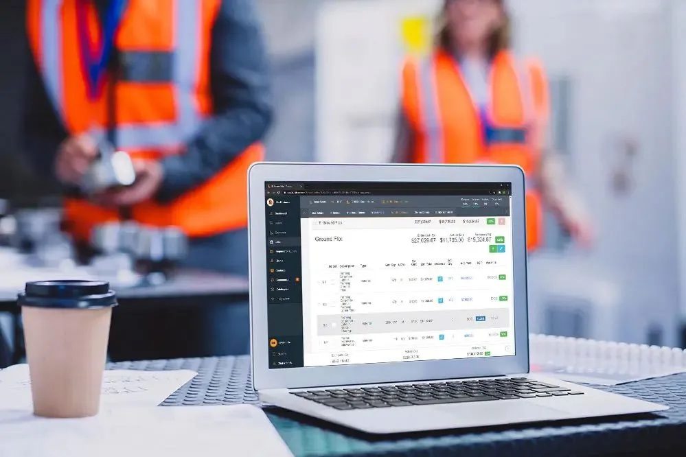 Laptop showing Buildxact's software on construction site with workers in the background