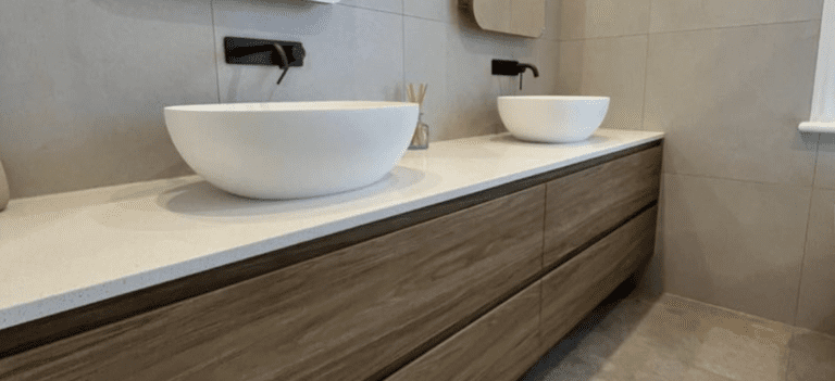 Two white bathroom sinks on a walnut timber floating vanity with marble stone counter tops.