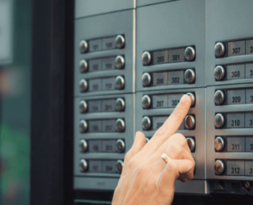 A finger pressing an apartment call button on the buzzer