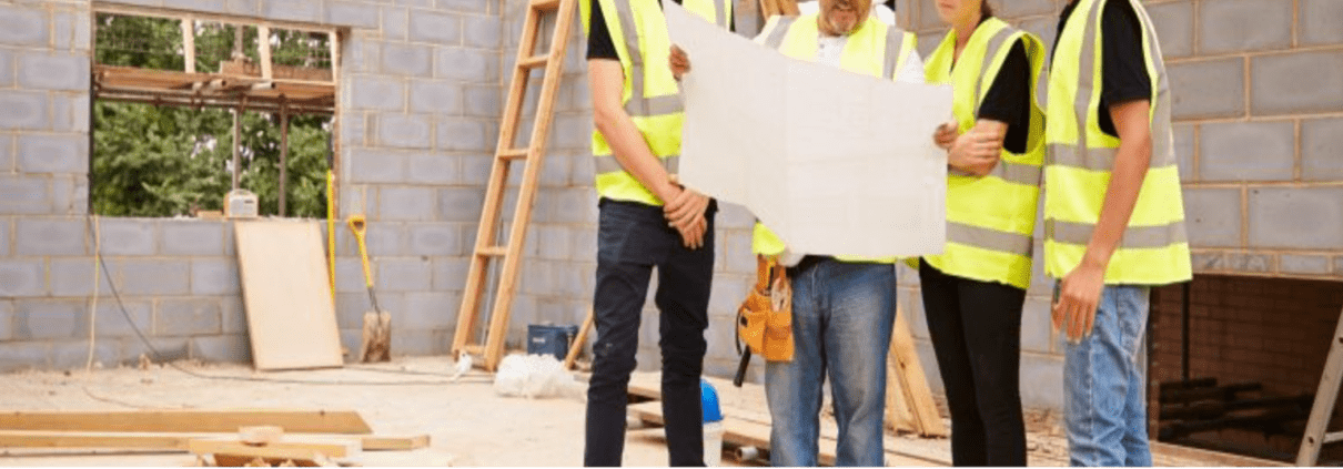 4 Tradies in high vis vests are in the middle of a construction site consulting a large paper plan