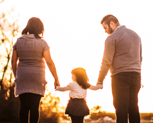 Mum and Dad hold hands with their child walking into the sunset