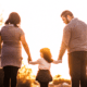 Mum and Dad hold hands with their child walking into the sunset