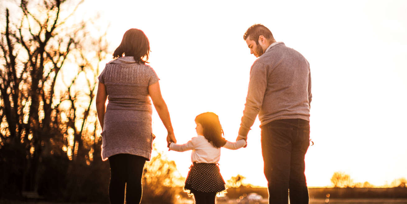 Mum and Dad hold hands with their child walking into the sunset