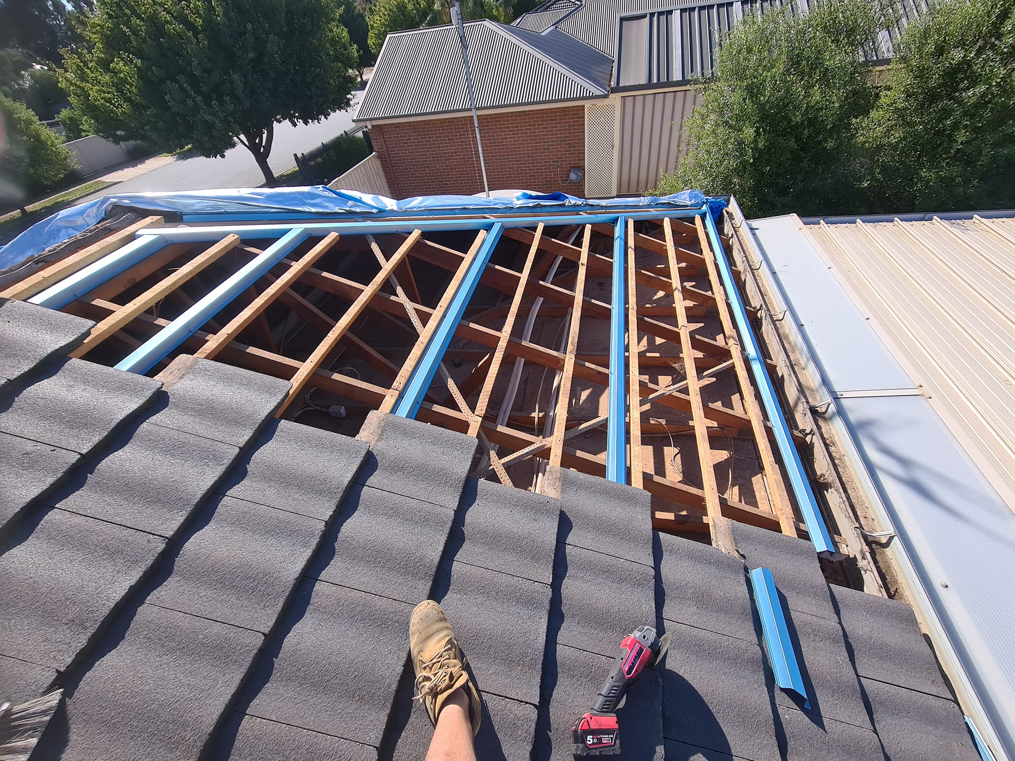 Worker on roof with half roof tiles complete and the other half timber and pipes exposed