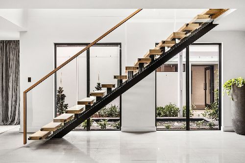 White house with floating timber stairs on black steel frame. Glass balustrade with a timer handrail