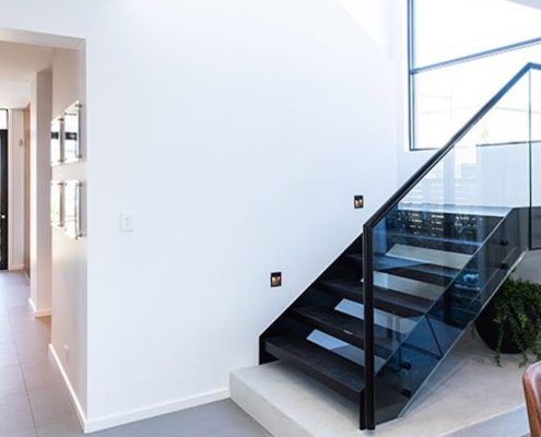 Black steel stairs with glass balustrade and matching black steel l handrail leads into a dining space with a long hallway to the front door.