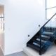 Black steel stairs with glass balustrade and matching black steel l handrail leads into a dining space with a long hallway to the front door.