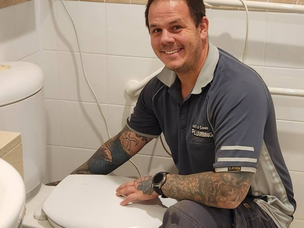 MT & Sons Plumber fixing toilet and smiling at camera
