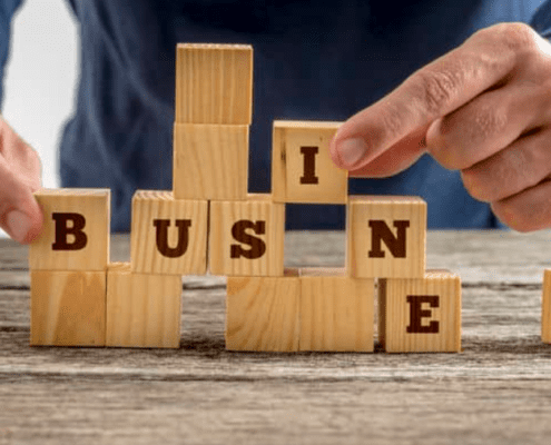 Hands playing with little wooden blocks on a table spelling out “business”