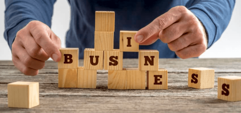 Hands playing with little wooden blocks on a table spelling out “business”