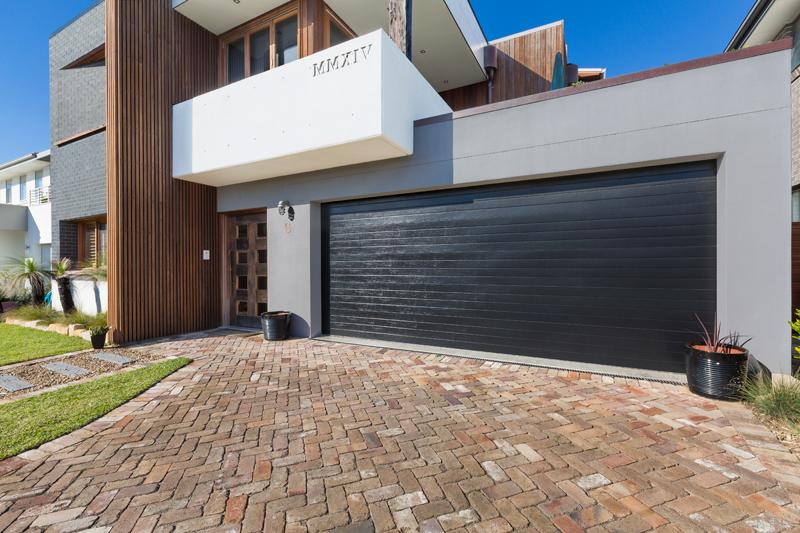 Modern architectural home with vertical timber cladding, black brick and large black garage door