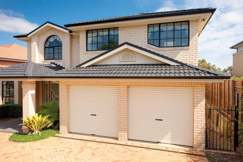 White brick house with black roof tiles and two surfmist roller garage doors