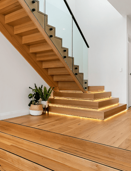 Modern timber stairs with glass balustrade and black hardware. Bottom steps are large squares with led light strips around the edges