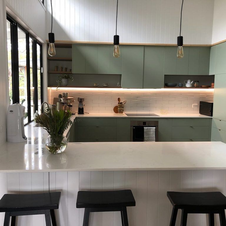 White kitchen with green cabinets and black accented lights and kitchen island stools