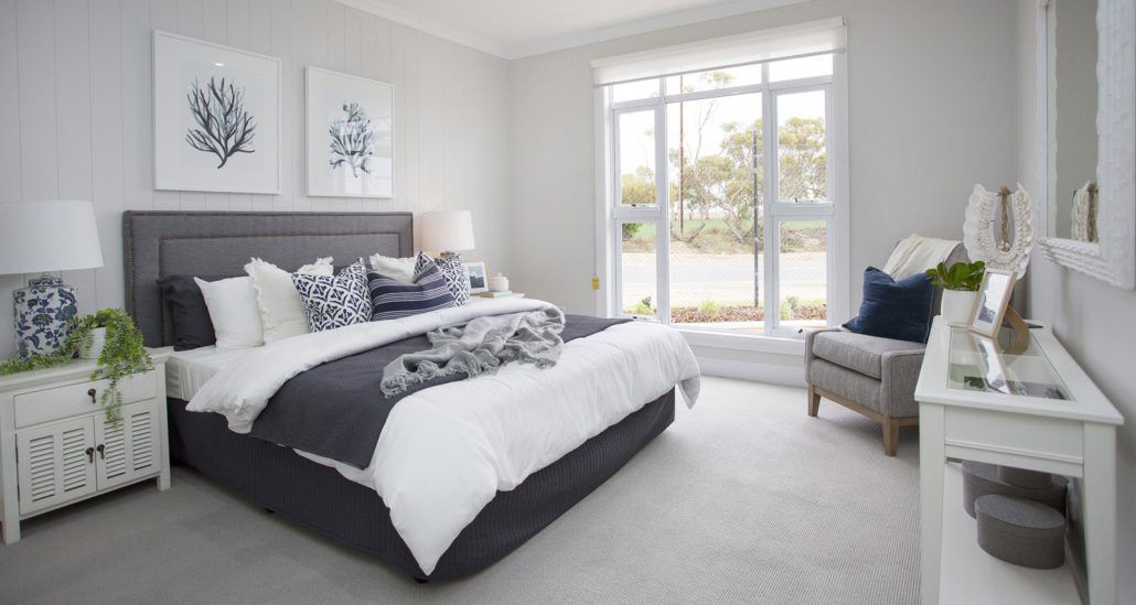 Bedroom with big grey bed in the middle and a large awning windows looking out to the garden