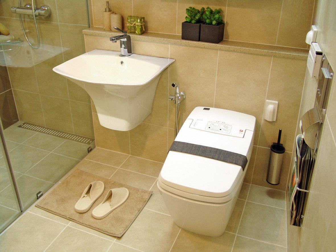 Beige tiled bathroom with white faucet and toilet. Slippers on the bath mat in front of the faucet.