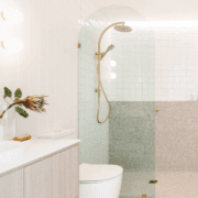 Light and bright bathroom with an arched glass shower screen and a high rainfall shower head. White toilet and vanity