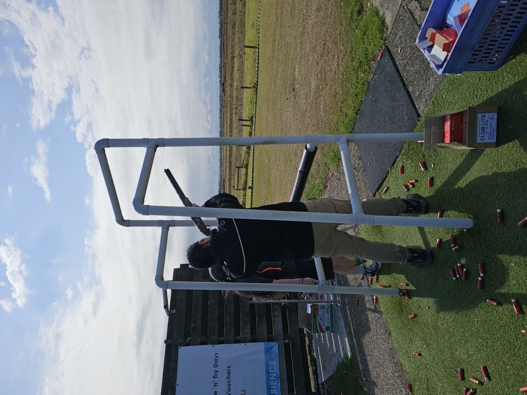 Member aiming gun at the sky at clay shooting day with instructor hidden next to him