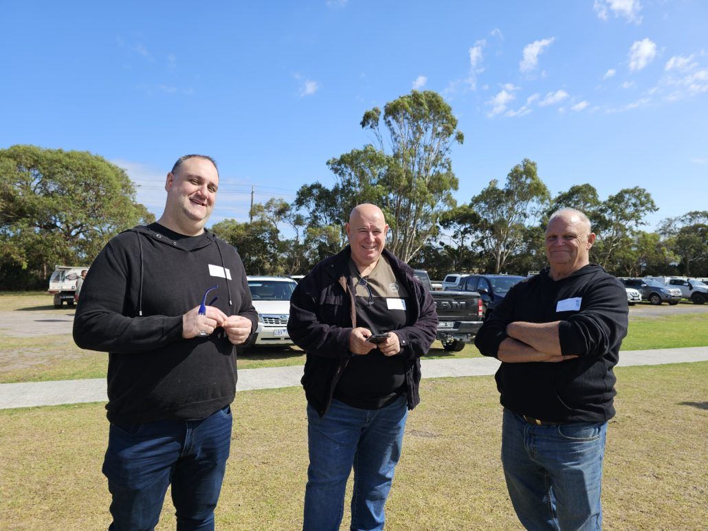 TAG members at our clay shooting event smiling at the camera in front of a carpark and blue sky