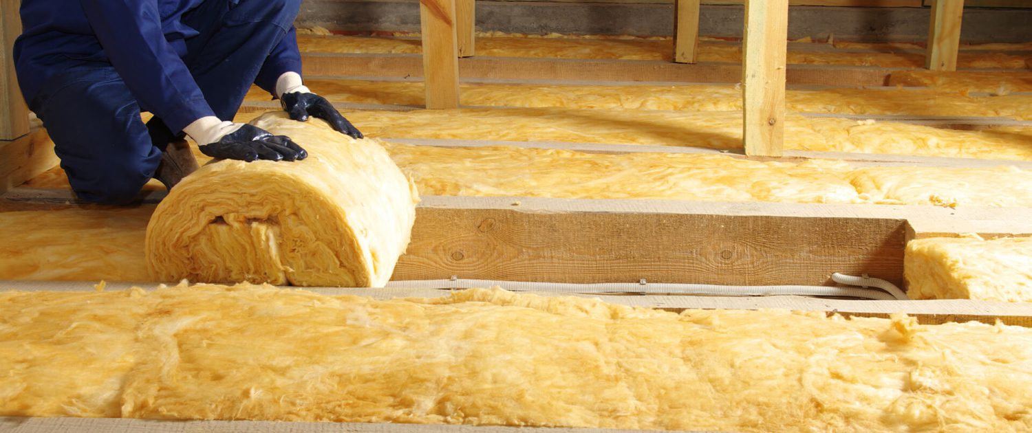 Man in attic rolling out insulation with gloves on