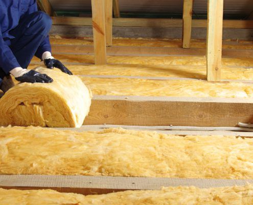 Man in attic rolling out insulation with gloves on