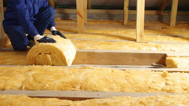 Man in attic rolling out insulation with gloves on