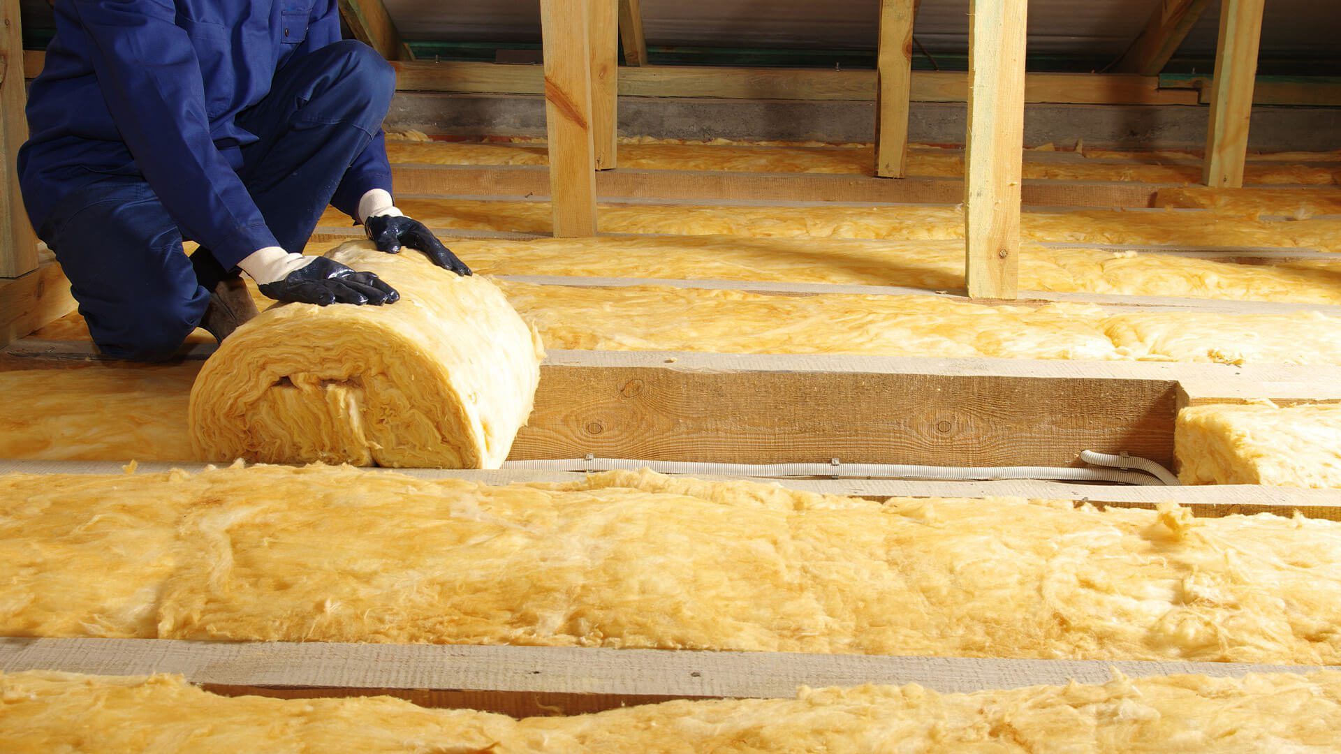 Man in attic rolling out insulation with gloves on