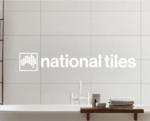 Bathroom with big standing bath and white tiles with a logo over the top with white text “National Tiles”