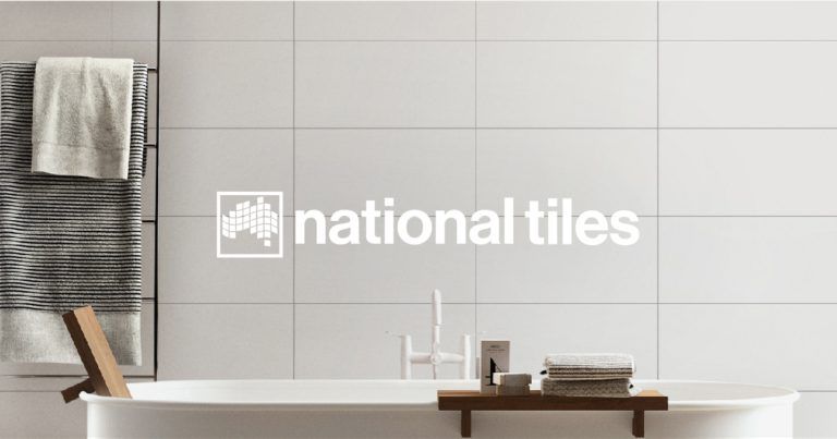 Bathroom with big standing bath and white tiles with a logo over the top with white text “National Tiles”