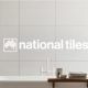 Bathroom with big standing bath and white tiles with a logo over the top with white text “National Tiles”