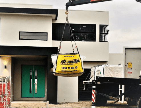 Jumbocorp's big yellow JumboBag being lifted onto a truck outside of a residential construction site.