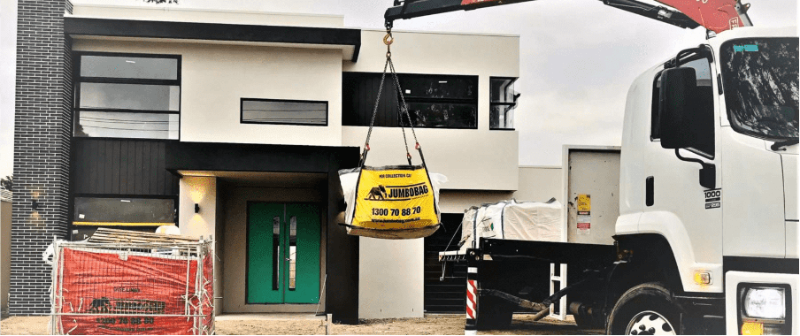 Jumbocorp's big yellow JumboBag being lifted onto a truck outside of a residential construction site.